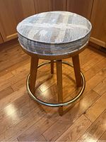 Angled side view of the padded stool showing cloth seat, wood legs, and brass foot rail on wood floor