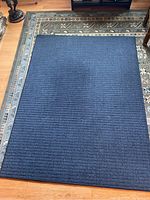 Blue rectangular floor rug placed on hardwood floor, showing full rug and surrounding area.