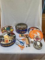 Overview photo of the four cookie tins and large array of sewing supplies including scissors, thread, and notions.
