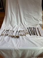 Full view of all cutlery pieces laid out on a white cloth background, including forks, cutters, large and small spoons, and serving spoons.