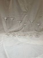 Full set of six tall clear glass votive candle holders shown in a row against cloth background highlighting size variation.