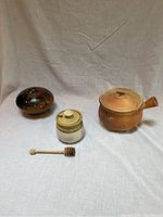 Three ceramic pots and wooden honey dipper arranged on white fabric backdrop, front view