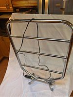 Front view of chrome-finished electrical towel warmer with 4 horizontal tubes and attached electrical cord.
