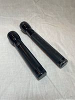 Two black Brinkmann metallic case flashlights, one smaller and smoother, one longer with textured grip, both with push button switches.