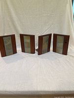 Four wooden bookends with metal blue and gold tiles positioned upright in a row on a white cloth.