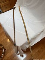 Two wooden walking sticks laid flat on a white cloth background, showing their full length and general shape.