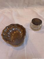 Photo showing both vintage sterling silver scallop shell bowl and cut glass jar with sterling silver cap on white fabric background.