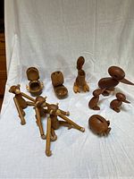 Photo showing all wooden animals together on a white cloth background including monkeys, ducks, pelican, hippo, whale, and piggy bank.