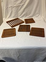 Five wooden trivets on white fabric background showing shape and design