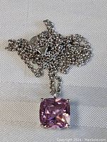 Photo of the pendant with pink square cushion-cut stone on a sterling silver chain, placed on white fabric.