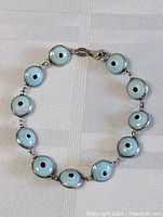 Full view of the 7-inch evil eye bracelet showing all nine linked charms, circular blue enamel with black and white eye detailing, and silver-tone metal connectors and clasp.
