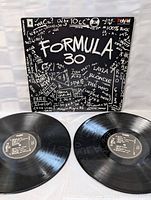Photo showing two vinyl records and part of the front cover of Formula 30 double LP set with black and white graphics and artist names.