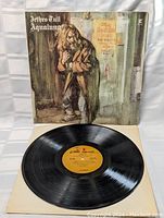 Photo showing vinyl record with orange label and original cover upright behind it.