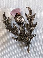 Close-up image of silver thistle pin showing textured detailed leaves and amethyst stone in flower head