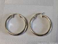 Pair of sterling silver hoop earrings shown on neutral fabric background, highlighting the polished surface and clasp closure.