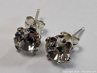 Close-up front angle of one sterling silver stud earring with a round clear faceted stone held in a silver four-prong setting, showing sparkle and condition.