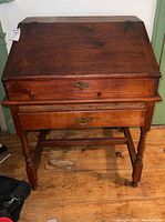 Front view showing slanted hinged top, drawer and turned legs