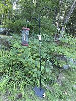Full view of black metal shepherd's hook standing in garden with bird feeder hanging from curved top.