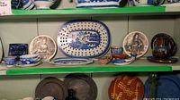 Shelves with an assortment of blue and white pottery, including pierced oval dish, bowls, cups, decorative black and white plates, brown jug, and metal plates below