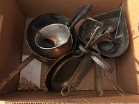 Box containing a variety of copper pots, kitchen utensils, and small pans.