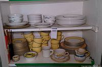 Shelf containing stacked Portmeirion The Queen's Hidden Garden bowls and plates along with stacked yellow Pagnossin Ironstone cups and plates