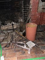 Overall fireplace accessory lot showing various andirons, shovel, wooden blocks, metal bucket near brick hearth