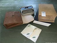 Overview of all items in the lot including typewriter, leather case, two dictionaries, and stationery packs