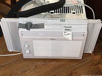 Front view of the white Midea window air conditioner unit with two control knobs. Unit shows signs of use and needs cleaning.