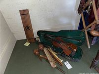 Overview of musical instrument lot showing violin in case, lap harp, flutes, and maracas grouped on floor corner.