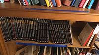 Shelf of Myth and Mankind book series showing a collection of around 30 hardcover books with black spines and gold/white text.
