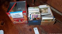 Boxes and tins containing many postcards neatly stored, including a metal tin, cardboard boxes with postcards arranged inside.
