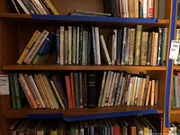 Wide view of multiple wooden shelves filled with assorted vintage hardcover and paperback books showing various spine colors and worn conditions.