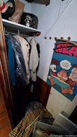 Closet area showing hanging coats and a glimpse of plaid fabric on the floor, plus a Garfield poster on the wall.