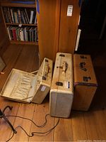 Three vintage suitcases on wooden floor, one open showing interior elastic compartments