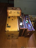 Photo showing four vintage suitcases stacked and standing on wooden floor with visible wear and leather handles.