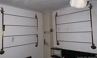 Pair of vintage brass towel racks mounted on wall, each with four horizontal bars and mounted in corners of a room.