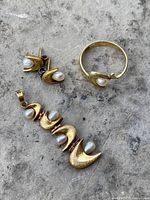 Set of 925 sterling silver earrings, pendant, and ring arranged on a stone surface showing textured gold-tone finish and freshwater pearls