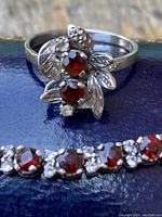 Close-up of ring cluster design with two garnets and clear accents alongside bracelet gemstones