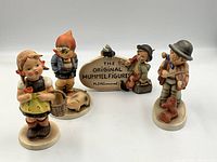 Four Hummel porcelain figurines grouped together on a plain background, showing the front view of each figure.
