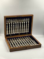 Full view of original wooden box with lid open, showing 12 forks on the top tier and 11 knives on the bottom tier