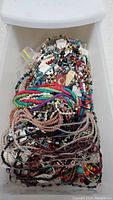 Drawer container filled with assorted colorful handmade beaded necklaces and bracelets, displaying a variety of bead colors and shapes packed together.