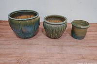 Front view of three glazed fishbowl planter pots in earth tones arranged side by side on wooden floor.