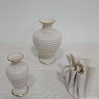 Two Lenox Athenian Collection vases of different sizes next to a white wrinkle ceramic vase by Carol Berclay on a white quilted surface.