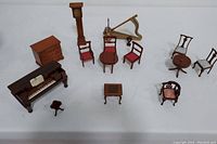 Overview photo showing entire lot of miniature classical dollhouse furniture and musical instruments arranged on white surface.