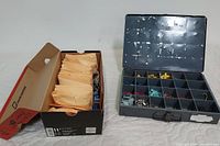 Metal box with multiple compartments holding various insulated quick connect terminals, adjacent to a shoebox with envelopes of electrical supplies.