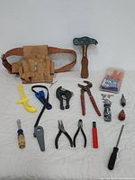 Photo of the lot showing leather toolbelt and various hand tools spread out on white sheet