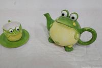 Tea pot and mug with saucer shown together on white cloth background.