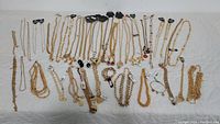 Photo showing the full assortment of gold metal necklaces and bracelets laid out on a white surface, showcasing various chain styles and pendants.