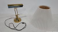 Vintage gold bankers desk lamp with round base, adjustable arm, and rectangular shade; cord attached.