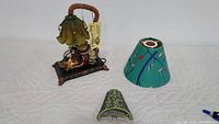 Table lamp with beaded frog, scalloped green glass shade, amber bead accents, and rectangular base with gold trim. Includes small teal colored fabric lampshade with fishing lure design and small green beaded metal night light shade with bead details.